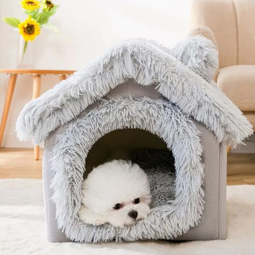 Cabane pour chien grise en forme de maisonnette, avec revĂȘtement doux et intĂ©rieur moelleux, un cocon de confort et de sĂ©curitĂ© Ă  un petit chien blanc allongĂ© Ă  lâentrĂ©e.