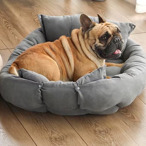 Canapé pour chien rond gris moelleux avec coussins intégrés, offrant confort et soutien à un bouledogue français heureux.