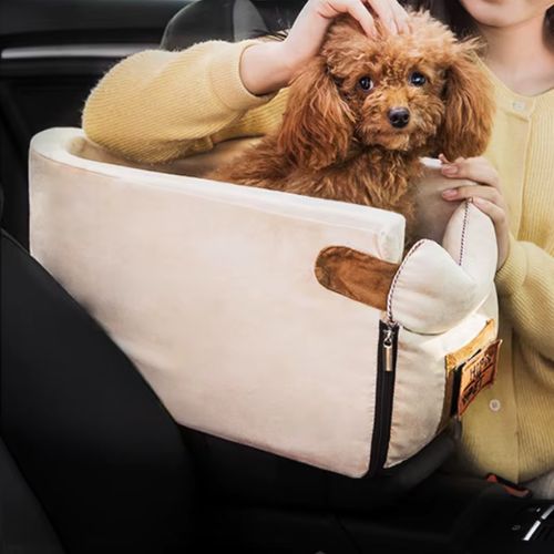 Petit chien assis dans un lit pour chien auto beige, sécurisé et confortable, utilisé lors d’un trajet en voiture avec son maître