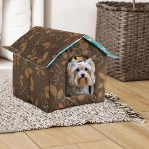 Un Yorkshire allongé confortablement dans une niche pour chien extérieur marron design cocon chaud.