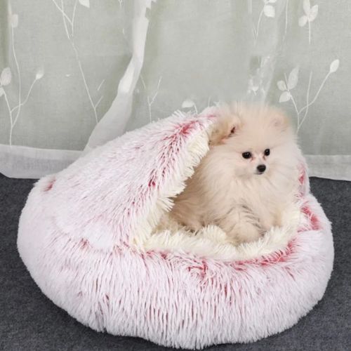 Petit chien blanc confortablement installé dans un panier chien rose en forme de nid douillet, dans une chambre chaleureuse.