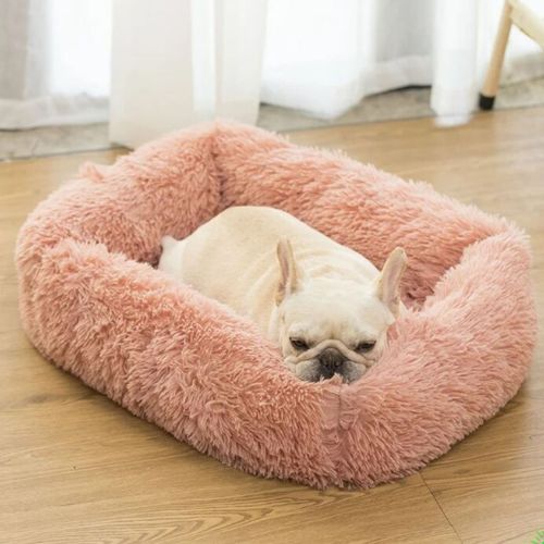 Un bouledogue français blanc se repose tranquillement dans son coussin pour chien moelleux, rebord surélevé, format rectangle couleur rose.
