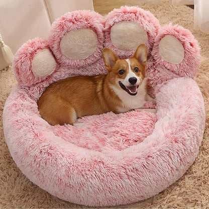 Petit chien marron installé confortablement sur un coussin pour chien format patte d'ours rose doux et moelleux