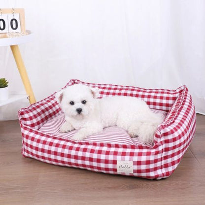Petit chien couché dans un panier pour chien moelleux en tissu vichy rouge, placé dans un intérieur lumineux