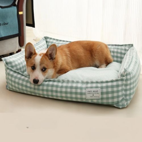 Petit chien couché dans un panier pour chien moelleux en tissu vichy vert, placé dans un intérieur lumineux