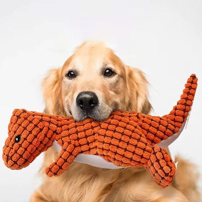 Golden Retriever tenant fièrement dans sa gueule une peluche pour chien dinosaure orange en tissu texturé.