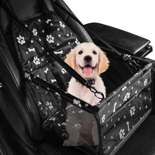 Un petit Labrador assis confortablement dans un siège auto pour chien noir avec motif patte et os.